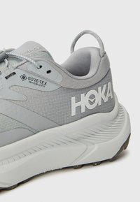 Grå HOKA løpesko med et teksturert mesh-overdel, GORE-TEX-merke, polstret krage, reflekterende detaljer og en dempet såle.
