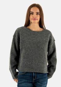 Maglione grigio in lana con un ampio scollo e spalle scese. Texture morbida, maniche lunghe e vestibilità rilassata. Abbinato a jeans blu.