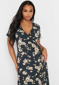 Vaatetettu mekko lyhyillä hihoilla, tummansininen kangas, jossa on suuria beigejä kukkakuoseja, v-kaula-aukko ja sidottu vyötäröyksityiskohta.