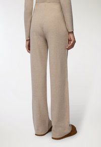 Beżowe spodnie dzianinowe z prążkowanej dzianiny o rozkloszowanym kroju, z teksturowanym wykończeniem i wysokim stanem, noszone z brązowym obuwiem.