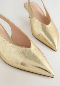Zapatos de tacón tipo slingback dorados con punta afilada, acabado metálico agrietado y un tacón pequeño. El interior cuenta con un forro suave de color nude.