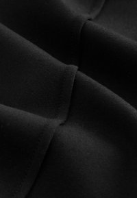 Prim fabric negru în prim-plan, cu o textură netedă, cu un ușor luciu și cusături vizibile de-a lungul marginilor. Forme drapate curbe.