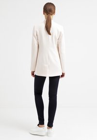 White blazer with a fitted design, two back vents, paired with black skinny jeans and white platform shoes. Simple, clean look.