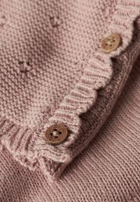 Pleteni izdelek v nežno rožnati barvi z teksturirano tkanino, s skobčanim robom in dvema lesenima gumboma z rožnatimi izrezi.