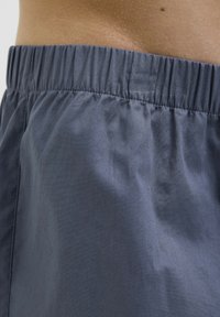 Shorts en tissu léger de couleur bleue avec une taille élastique, texture lisse et détails de couture minimaux. Vue rapprochée du côté.