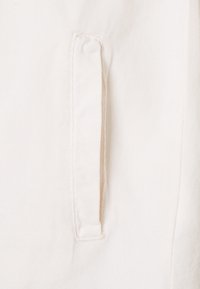 Vit bomullstyg med en texturerad yta som har en vertikal ficka sydd längs sömmen. Enkel och ren design.