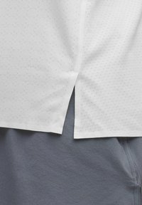 Witte korte mouwen shirt met een textuur stof met kleine stippen, split hem detail. Gecombineerd met grijze shorts, die een zachte textuur tonen.