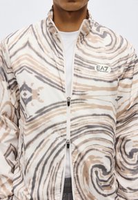 Ανδρικό ελαφρύ μπουφάν με φερμουάρ, με αφηρημένο μοτίβο στροβίλου σε μπεζ και γκρι αποχρώσεις και το λογότυπο EA7 Emporio Armani στο στήθος.