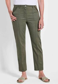 Olivgrüne, gerade geschnittene Hosen mit Fronttaschen und subtilen Nähdetails, kombiniert mit hellen Slippern.