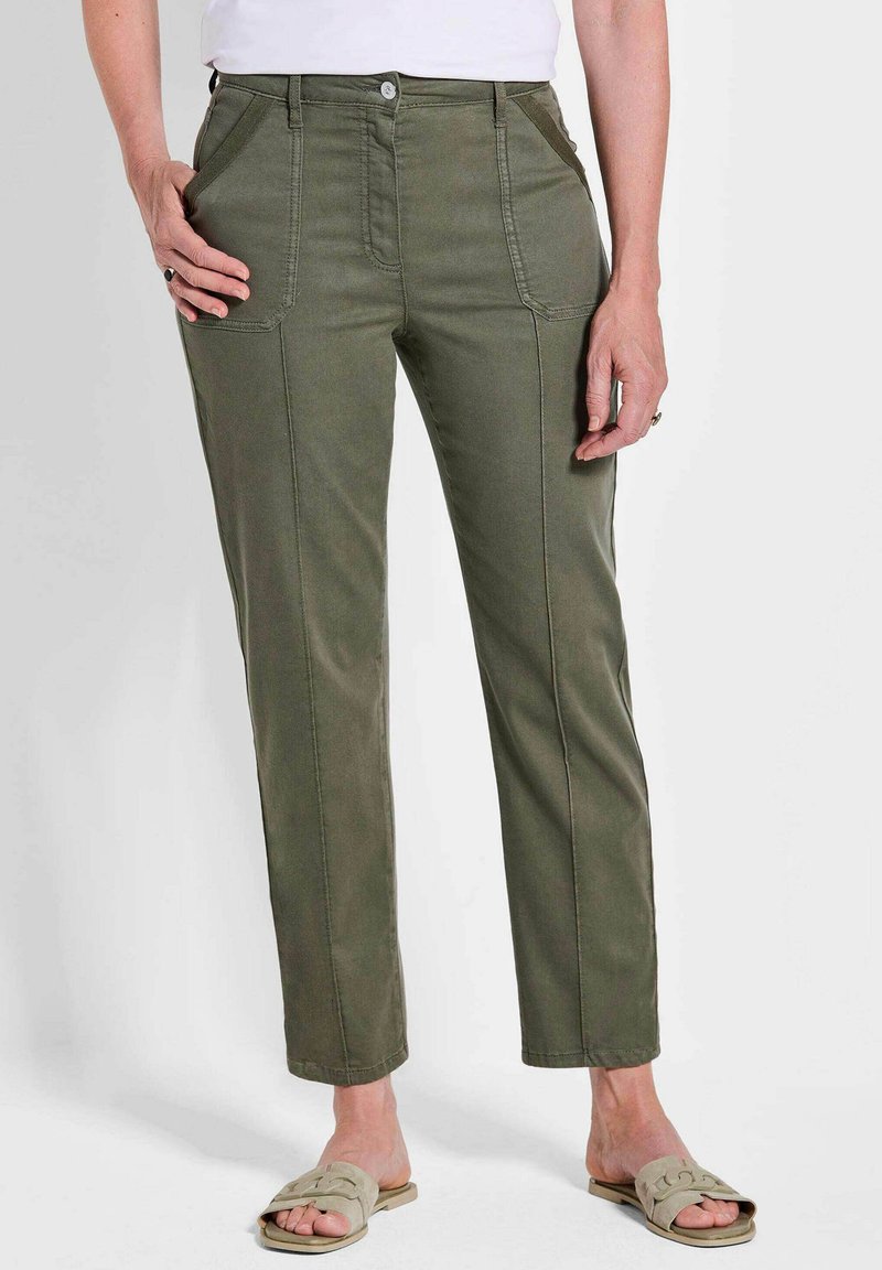 Olijfgroene, rechte broek met voorzakken en subtiele stikdetails, gecombineerd met lichtgekleurde instapschoenen.