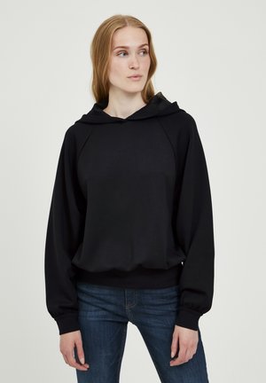 Schwarzer Kapuzenpulli mit langen, weiten Ärmeln und lockerer Passform. Mit gerippten Bündchen und glatter Textur. Getragen mit blauen Jeans.