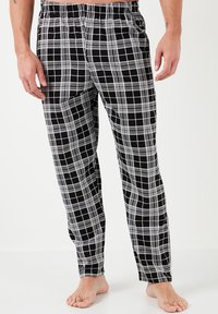 Pantaloni da pigiama in cotone con motivo a quadri, caratterizzati da una trama a griglia bianca e nera, vita elastica e vestibilità ampia. Senza tasche né bottoni visibili.