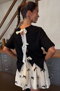 Svart kortärmad topp med en öppning bak som är knuten med ett krämfärgat band, kombinerad med en vit kjol dekorerad med svarta rosettmönster.