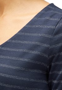 Top blu navy con un design a V, caratterizzato da sottili strisce orizzontali argento. Il tessuto appare morbido con una superficie liscia.