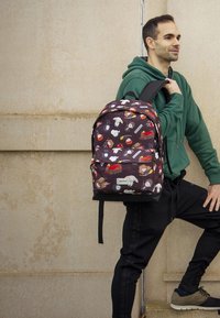 Mochila hecha de un tejido resistente en color púrpura oscuro con patrones de animales de dibujos animados coloridos, cuenta con correas de hombro acolchadas y un bolsillo frontal.