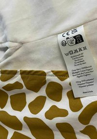 Tkanina bawełniana o białej podstawie z brązowym wzorem w plamy żyrafy. Przypięta metka z instrukcjami prania i szczegółami materiału.