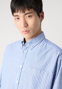 Blau-weiße gestreifte Button-Down-Bluse mit einer unauffälligen Tasche, ausgestattet mit einem Kragen und einem leichten Stoff.