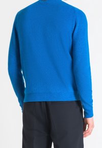 Pull bleu tricoté avec une texture côtelée, col rond et manches longues, associé à un pantalon noir. Vue arrière montrant la coupe et la couleur.
