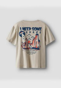 Beżowy bawełnowy t-shirt z kolorowym graficznym wzorem przedstawiającym góry, tekstem "POTRZEBUJĘ TROCHĘ PRZESTRZENI" oraz ilustracją UFO.