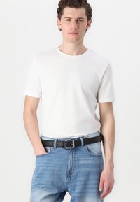 Camiseta blanca de algodón con cuello redondo, manga corta, combinada con unos vaqueros de denim azul claro y un cinturón de cuero negro.