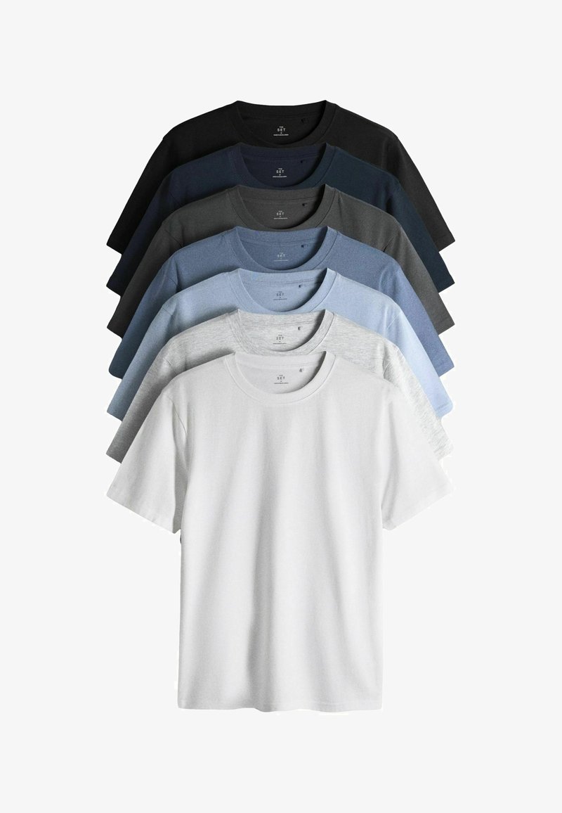 Sette t-shirt semplici a maniche corte con scollo rotondo, disposte in una gradazione dal bianco al nero, includendo tonalità di grigio e blu.