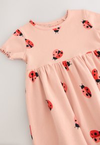 Rosa ribbad klänning med röda och svarta nyckelpige-tryck, korta ärmar med rynkade detaljer och en kjol med utsvängd design.