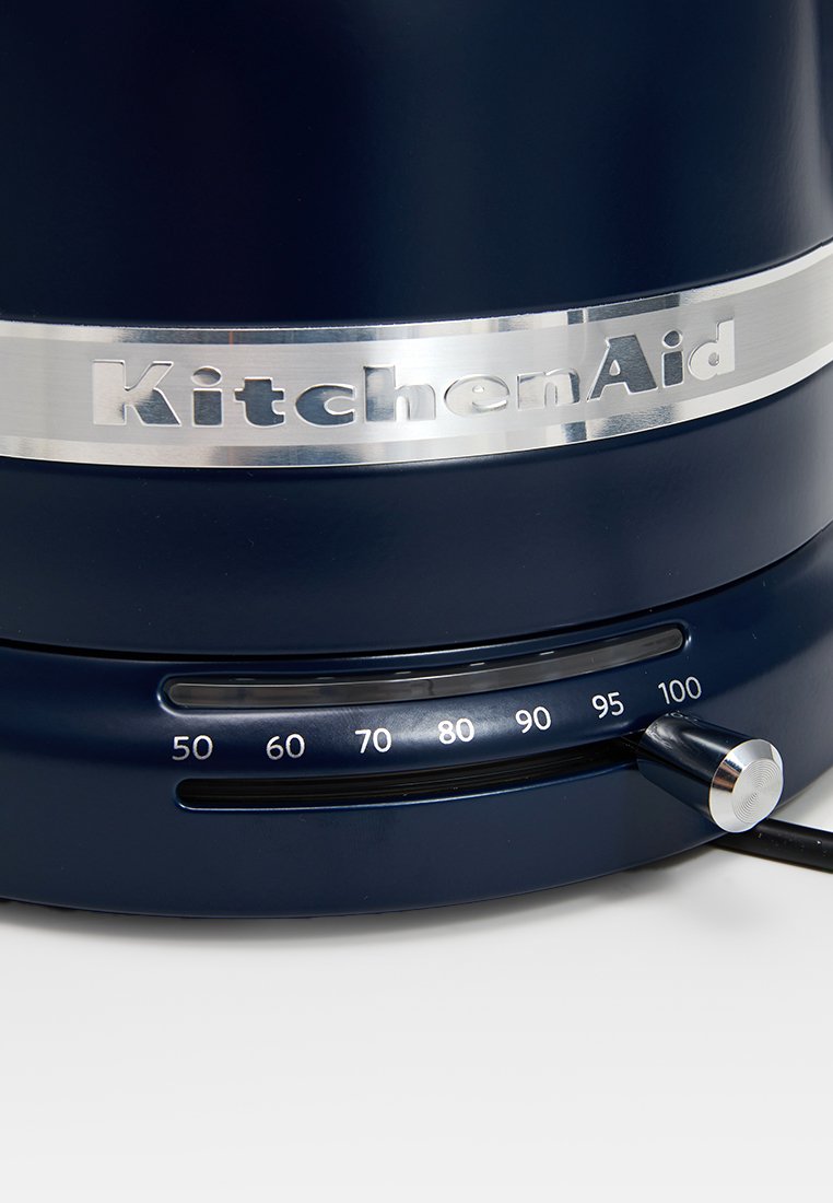 Marineblaue KitchenAid-Gerät mit einem metallischen Band, das das Logo zeigt, und einem Steuerknopf, der mit Zahlen von 50 bis 100 für die Einstellungen gekennzeichnet ist.