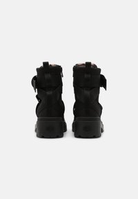 Botas de tobillo negras con parte superior de tela texturizada, correas ajustables y suela de goma gruesa. Presenta una cremallera en el costado para ponerlas y quitarlas fácilmente.