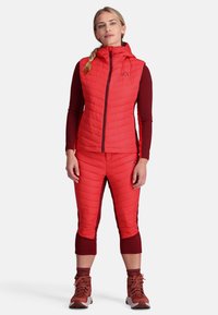 Rote isolierte Weste mit Kapuze und Reißverschluss vorne, kombiniert mit passenden, kurzen Hosen. Das Outfit verfügt über ein strukturiertes Design und eine figurbetonte Passform.