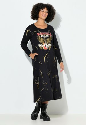 Schwarz langärmliges Kleid mit einem Grafikdesign des Nashville Music Festivals und goldenen Akzenten. Das Kleid hat eine lockere Passform und Taschen und wird mit schwarzen, klobigen Stiefeln getragen.