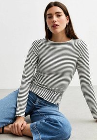 Langsleeve gestreept top in zwart en wit, met een ronde halslijn en een geschulpte zoom, gecombineerd met wijd uitlopende blauwe jeans.