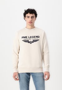 Bež dukserica dugih rukava s okruglim izrezom, s mornarsko plavimprintanim tekstom "PME LEGEND AMERICAN CLASSIC" i grafikom krila.