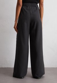 Zwarte wijde broek van stof met een elastische tailleband. Beschikt over subtiele zijzakken en een gladde textuur.