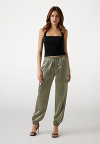Canotta nera arricciata abbinata a pantaloni cargo satinati verde oliva con polsini elasticizzati e tasche, indossata con tacchi a stiletto neri.