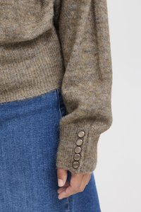 Brun stickad tröja med ribbad nederkant och långa ärmar, med fem runda knappar på muddarna. Matchad med blå denim.