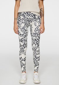 Leggings bianchi con un design a stampa animale nera, realizzati in tessuto elastico con una texture liscia. Abbinati a sneaker chiare.