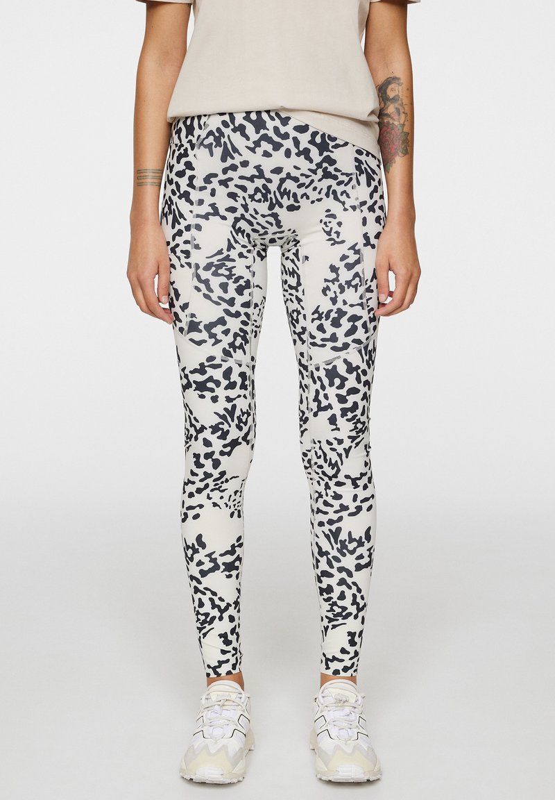 Leggings bianchi con un design a stampa animale nera, realizzati in tessuto elastico con una texture liscia. Abbinati a sneaker chiare.
