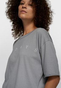 T-shirt en coton gris à coupe décontractée, avec des manches courtes et le mot « DAYS » imprimé en blanc sur la poitrine.