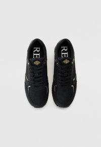 Zapatillas negras con material texturizado, diseño de cordones, detalles perforados y acentos de logotipo dorado en la lengüeta y los laterales.