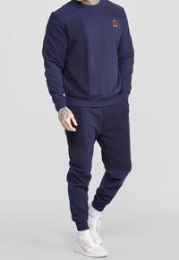 Sudadera azul marino y joggers a juego confeccionados en una tela suave, con variaciones de textura, puños acanalados y un pequeño logo bordado en el pecho.