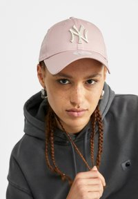 Pink baseball cap with embroidered NY logo on the front. Smooth fabric with a curved visor, worn with a gray hoodie.