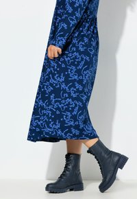 Laivastonsininen mekko, jossa on käsinkirjoitustyylistä sinistä kuviota, yhdistetty tummansinisillä nyörillä varustetuilla taistelukengillä ja hieman kellotetulla siluetilla.