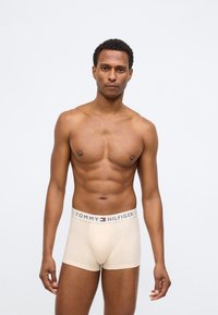 Μπεζ μποξερ σλιπ από μαλακό ύφασμα με άνετη εφαρμογή. Διαθέτει λαστιχένια μέση με το όνομα "TOMMY HILFIGER" σε έντονα γράμματα και τονίσματα του λογότυπου.