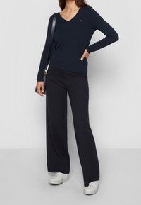 Maglietta a maniche lunghe blu navy con scollatura a V e vestibilità slim, abbinata a pantaloni larghi blu navy e sneakers bianche. Design semplice con accenti minimi.