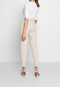 Pantaloni alta vita beige con una vestibilità affusolata e tasche posteriori, abbinati a una camicia bianca e a scarpe con tacco a fantasia.