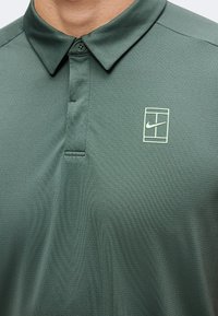 Polo vert à col avec un petit logo Nike blanc et un design rectangulaire sur la poitrine gauche, fabriqué en tissu texturé et respirant.