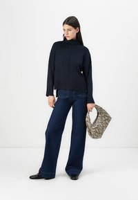 Navyblauer gestrickter Rollkragenpullover mit gerippter Textur, kombiniert mit weiten dunklen Jeans und einer snake-angeleihen Handtasche.
