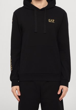Zwarte hoodie met voorzak en trekkoorden, gouden "EA7 Emporio Armani" logo op de borst en gouden merkopdruk op de linker mouw.