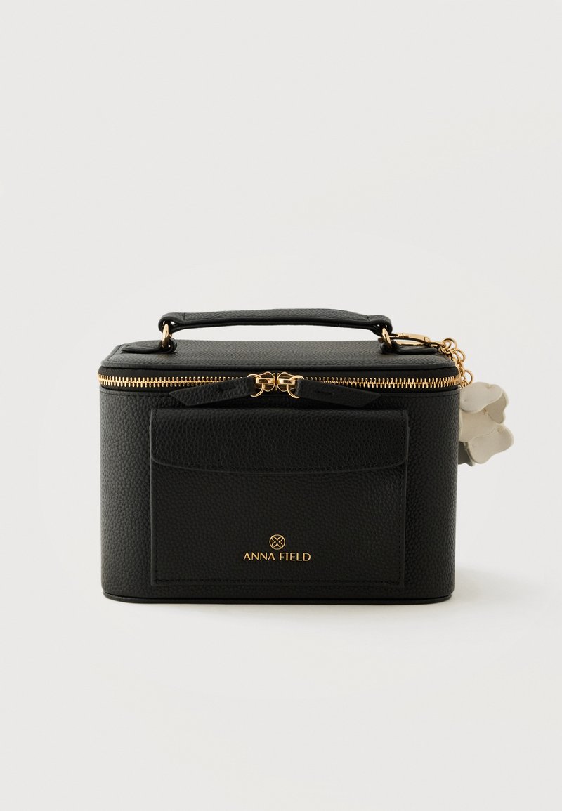 Sac à main rectangulaire noir texturé avec fermeture éclair dorée, poche avant, poignée supérieure et porte-clés fleur blanche.