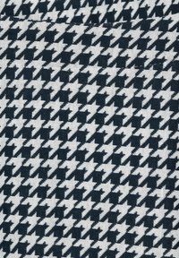 Tessuto a motivo houndstooth in bianco e nero, tessitura testurizzata, che presenta un design a zigzag ripetuto con angoli acuti su uno sfondo chiaro.